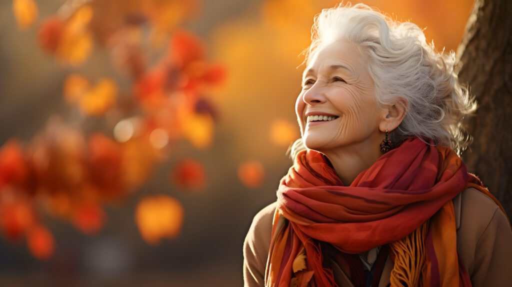 Portrait of an elderly happy smiling woman in autumn park, positive cheerful aged lady enjoying a walk outdoors in autumn forest